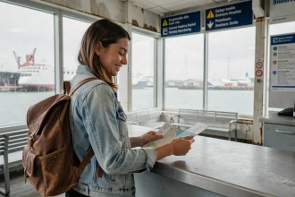 Jeune voyageuse française au comptoir d'embarquement d'un ferry pour l'Irlande, tenant ses billets et une carte routière